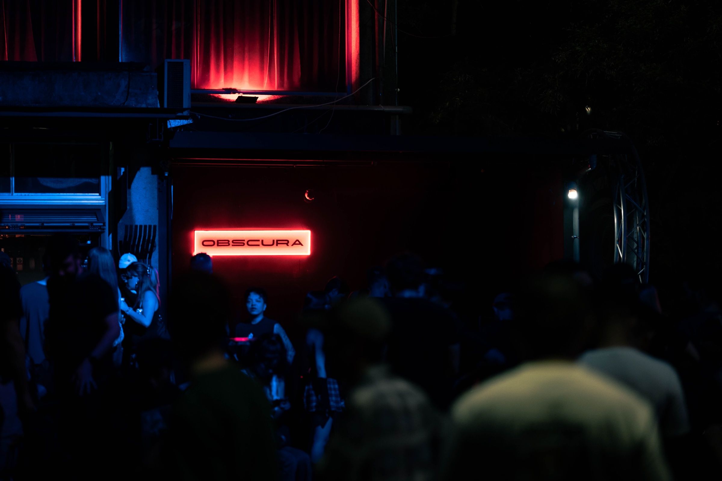 The entrance at night, guests beneath the red OBSCURA neon sign